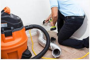 Contractor with various tools cleaning dry vent, with duct pipe removed and laying on the floor next to vacuum. 
