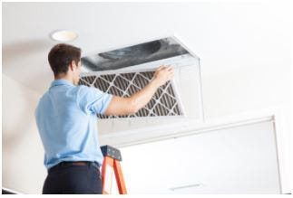 Man on ladder holding filter in front of open ceiling vent