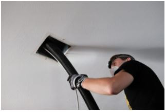 Professional air duct cleaner with vacuum tube inside white ceiling with duct.